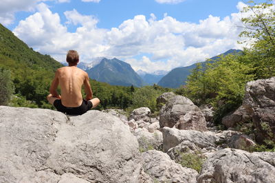 Rear view of man sitting on rock against mountains