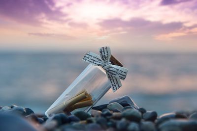 Close-up of bottle at beach against sky during sunset