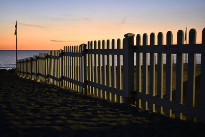 Wooden posts on beach against sky during sunset