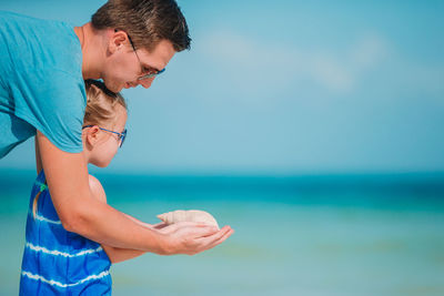 Side view of father and daughter holding seashell