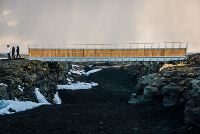 Bridge over rocks against sky during winter