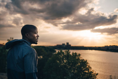 Male athlete looking away while standing on hill against sky during sunset