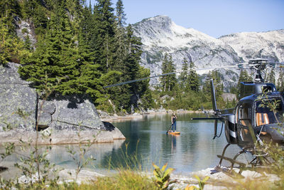 Active woman paddle boards on remote lake accessed by helicopter.