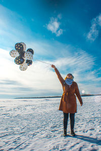 Woman with balloons standing on snow against sky