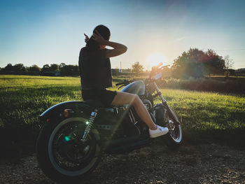 Woman sitting on motorcycle against sky during sunset