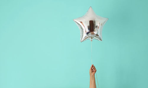 Cropped hand holding silver colored balloon against turquoise background