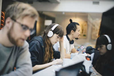 Female programmer working on computer with male colleagues at desk in office