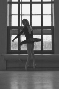 Side view of woman standing against window at home