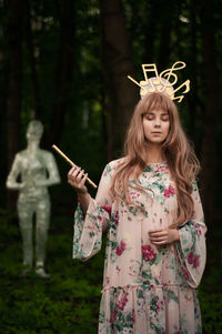 Woman in crown holding flute while standing against statue