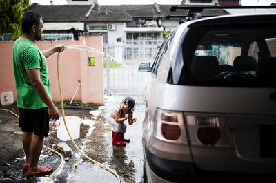 Playful boy looking at father cleaning car in yard