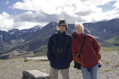 Portrait of father and daughter standing on mountain against cloudy sky during sunny day