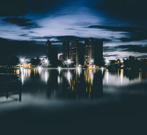 Idyllic view of illuminated city and river against cloudy sky during night