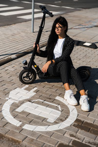 High angle view of woman with push scooter sitting on footpath