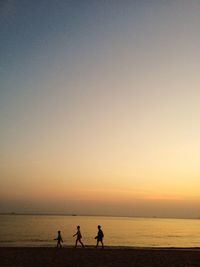 Silhouette boys walking at beach against sky during sunset