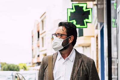 Mature man wearing face mask looking away against building