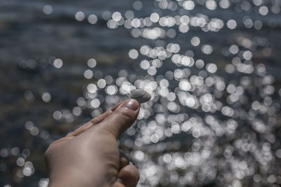A hand holding a seashell against blurred water