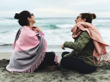 Young woman sitting on beach against sea