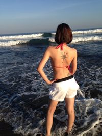 Rear view of sensuous woman standing on shore at beach