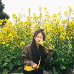 Portrait of young woman smelling yellow flowers growing on field