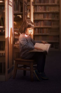 Girl reading book while sitting on chair at library