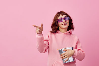 Portrait of smiling young woman taking selfie against pink background