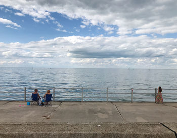 People sitting at sea shore against sky