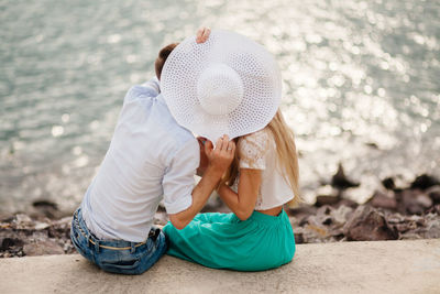 Couple with hat romancing on retaining wall by sea