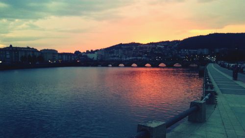 River by illuminated city against sky during sunset