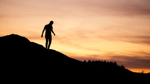 Silhouette man standing on mountain against orange sky