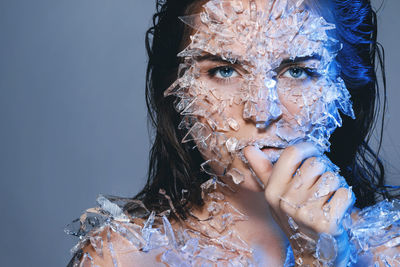 Portrait of woman with broken glass on body against purple background