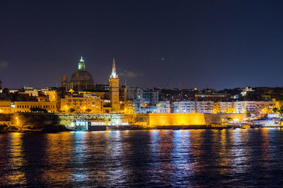 Illuminated cityscape by river against sky at night