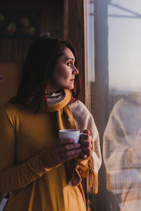 Woman with coffee looking towards window while standing at home