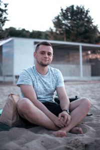 Portrait of young man sitting at beach during sunset