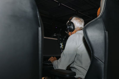 Rear view of elderly man playing game on computer while sitting on chair in gaming lounge