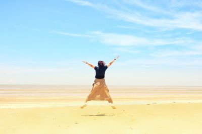 Rear view of woman jumping on sand at beach against sky