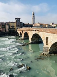 Arch bridge over river by buildings against sky