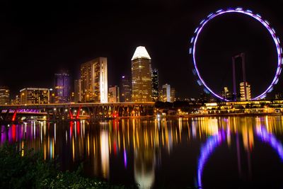 Illuminated buildings by river against sky at night