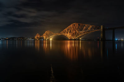 Illuminated bridge over river against sky at night