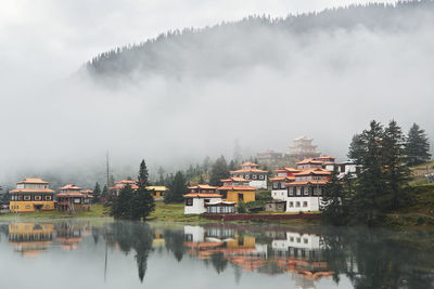 Scenery view of old buildings of tibetan buddhist temples located on shore of tranquil reflecting lake in highland covered with clouds