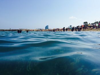 People swimming in sea against clear blue sky