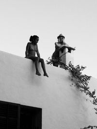 Low angle view of girl at retaining wall against clear sky