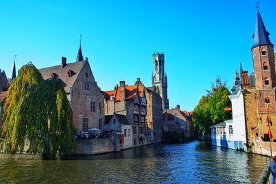 Canal amidst buildings against clear blue sky in city