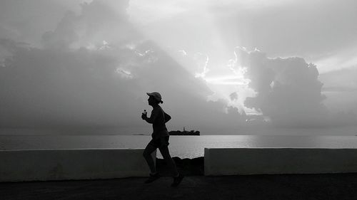 Side view full length of man jogging by sea on footpath against sky