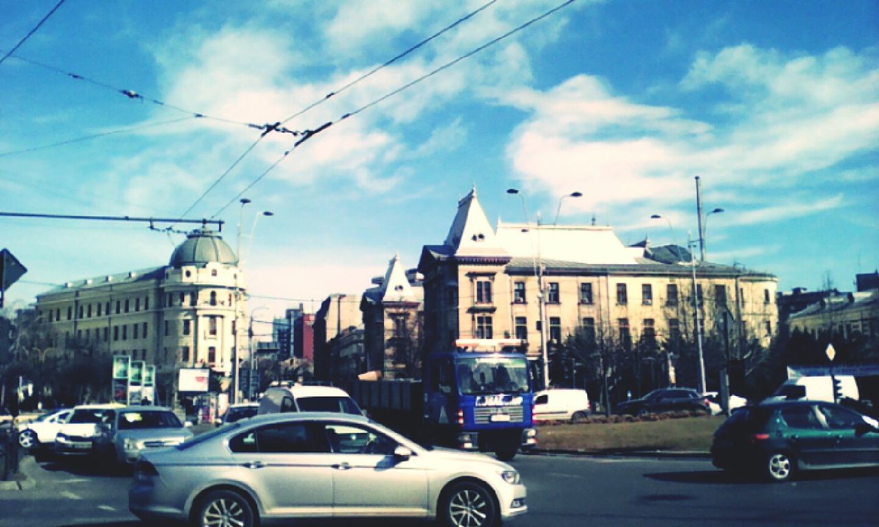 building exterior, car, land vehicle, sky, transportation, built structure, architecture, city, mode of transport, cloud - sky, street, road, city street, outdoors, city life, cable, no people, day, vehicle