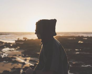 Side view of silhouette woman standing at beach against sky during sunset