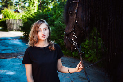 Portrait of young woman standing with horse against trees
