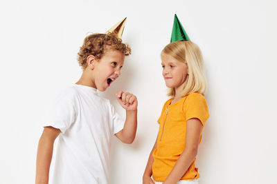Smiling brother and sister wearing party hat against white background