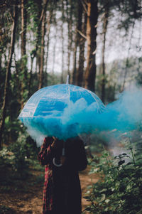 Woman with umbrella and blue smoke standing in forest