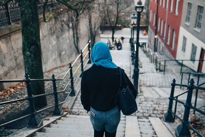 Rear view of young muslim woman moving down on staircase in city