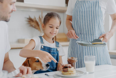 Midsection of parents looking at daughter making pancakes at home